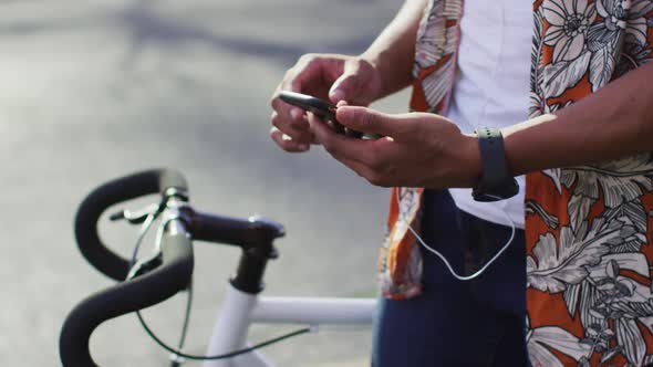 Midsection of african american man in city, with bike in street using smartphone