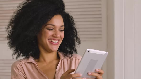 Cute African American Woman Looks Information on Digital Tablet and Happily Celebrates Victory