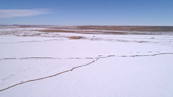 Flying over flat desert snowy landscape towards vehicle on road