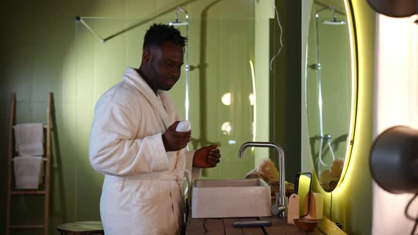Side View Positive Handsome African American Man in Bathrobe Turning on Music on Smartphone Applying
