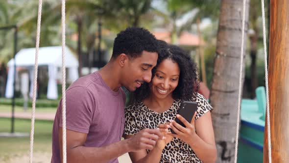 Cheerful Young Couple on a Swing Smiling Taking Selfie Photos with Smartphone