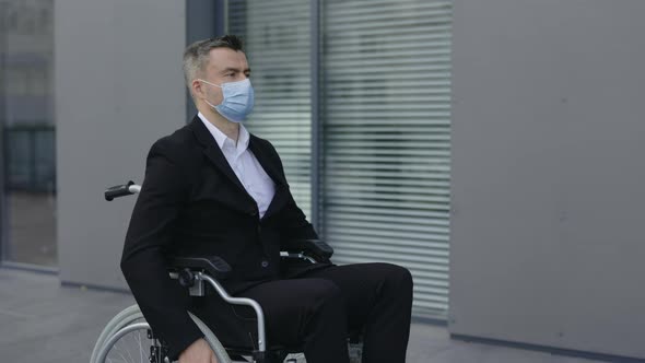 Side View of Stylish Guy in Protective Mask Riding in Wheel Chair and Looking Ahead at Street