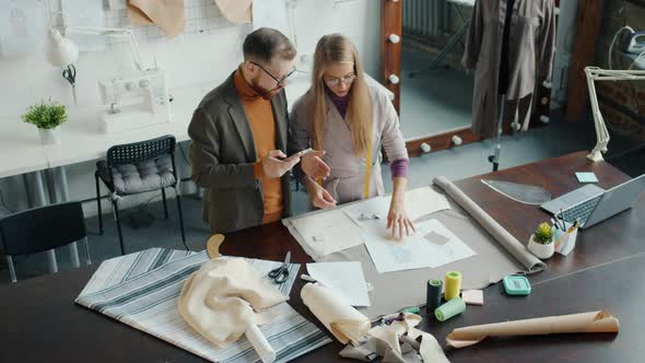 Creative Dressmakers Discussing New Collection Choosing Material and Using Smartphone at Work