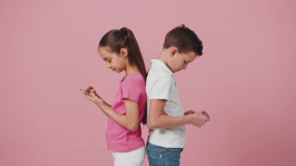 Little Boy and Girl Standing Back to Back and Networking on Smartphones Curious Sister Peeking Into