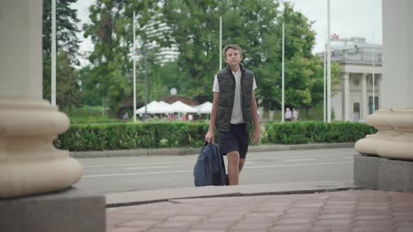 Portrait of Unhappy Schoolboy Approaching To Camera with Rucksack and Sighing. Sad Caucasian