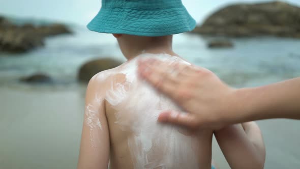 Mother Applying Sunblock Cream on Son Back at Beach.