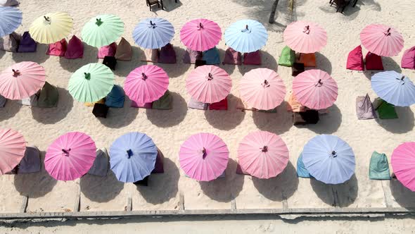 Aerial top down view of young girl lying at beach during summertime in front of colorful umbrellas.