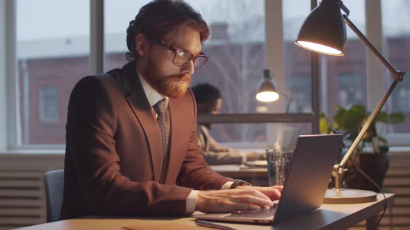 Caucasian Businessman Working on Laptop at Office Desk in the Evening