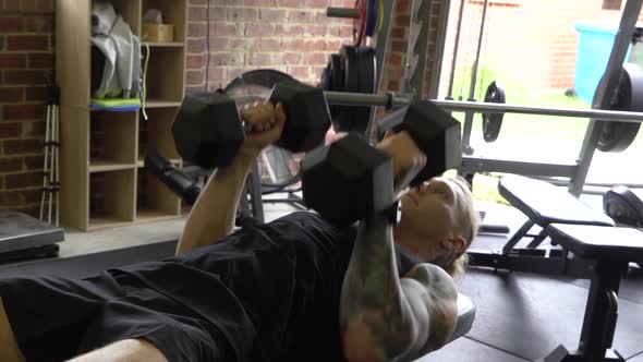 Muscly man in home gym exercising close grip dumbbell tricep press on bench
