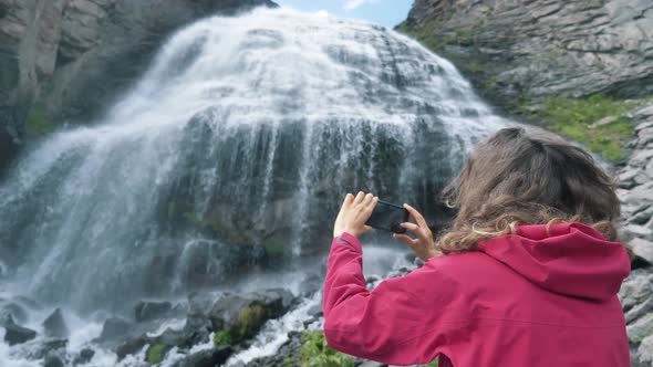 Lady Holds Phone and Makes Video Standing Near Waterfall