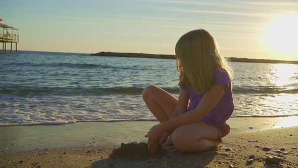 a Cute Little Girl Sits on the Seashore Playing in the Sand and with Pebbles