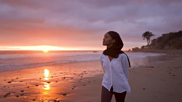 Somali-American woman walking on the beach at sunset