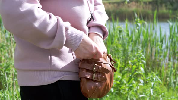 Female Takes a Lighter Out of Bag to Smoke in Nature Near a River with Reeds