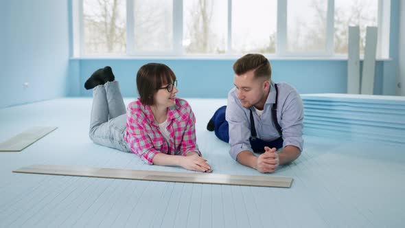 Woman and Man Lying on Insulated Floor Before Laying Laminate Rejoicing at Work Done Indoors