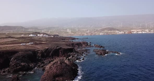 Beautiful coastline aerial view with cliffs and rocks and blue. Town and windmills in background.