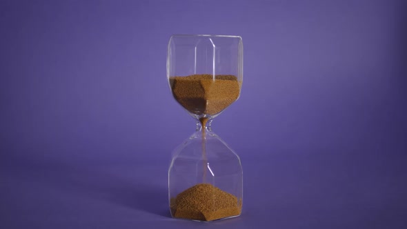 Glass Hourglass with Golden Sand on Purple Background