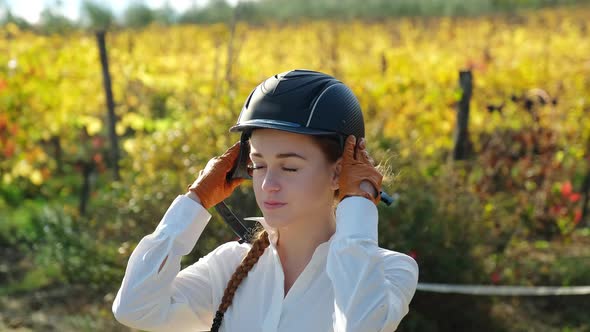 Young female rider putting on riding helmet