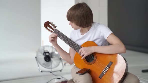 a Young Guy in a White Tshirt Learns to Play the Guitar