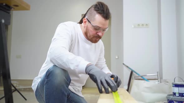 Carpenter in Protective Gloves and Glasses Makes Measurements on Wood