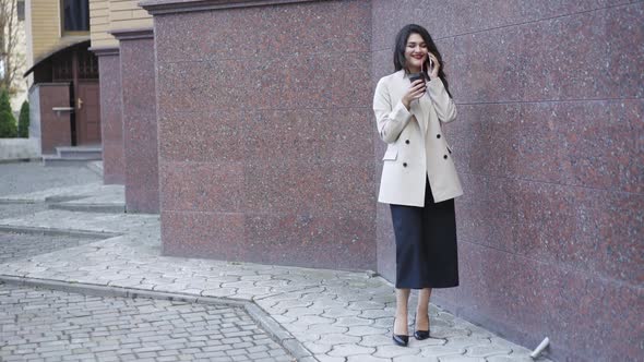 Playful Girl in Stylish Clothes Having Talk on Phone and Drinks Cup of Coffee