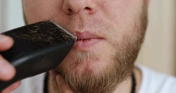 Handsome man in white t-shirts cutting beard, moustache personally himself with trimmer