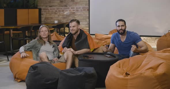 Wide Shot of Cheerful Multiethnic German Football Fans Sitting on Bean Bag Chairs and Cheering Win