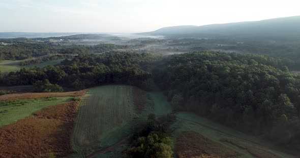 Aerial camera ascending view of West Virginia countryside with farms, fields, mountains and fog sett