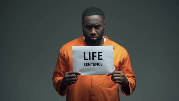 Afro-American Imprisoned Male Holding Life Sentence Sign, Looking to Camera