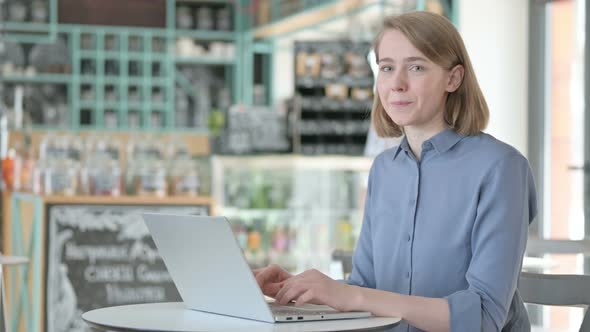 Young Woman Smiling at Camera While Working on Laptop