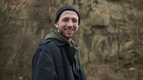 Stylish Young Guy Standing In Nature. Behind Him Is Rock. Guy Is Smiling.