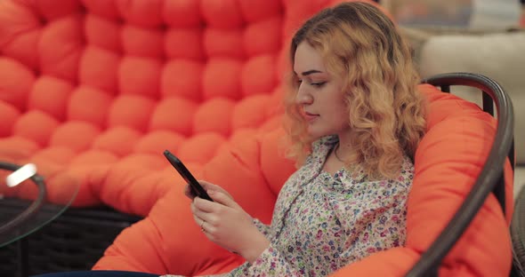 Woman Using Smartphone Sitting on Orange Sofa