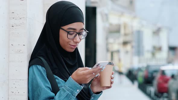 A beautiful arabian woman wearing national hijab is using her phone while drinking coffee