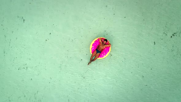 Aerial view of man floating on inflatable donut mattress, relaxing.