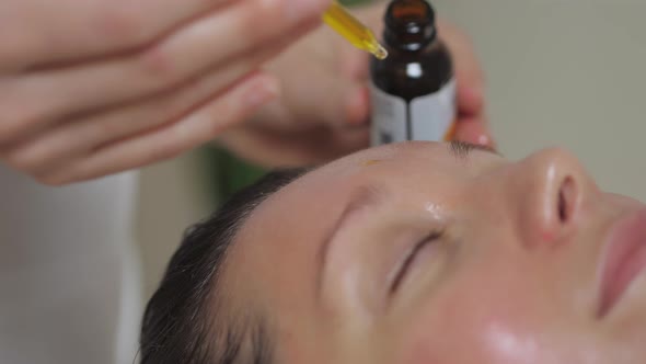 Applying Massage Oil on the Forehead of a Beautiful Brunette Woman in Spa Salon