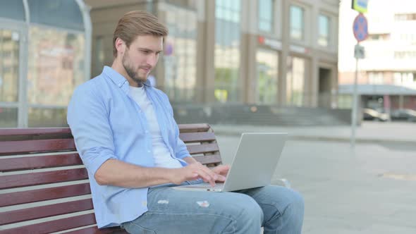 Man Celebrating Success on Laptop While Sitting Outdoor on Bench