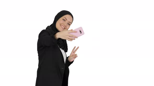 Smiling Arab Woman in Hijab Taking Selfies on Her Mobile Phone As She Walks on White Background