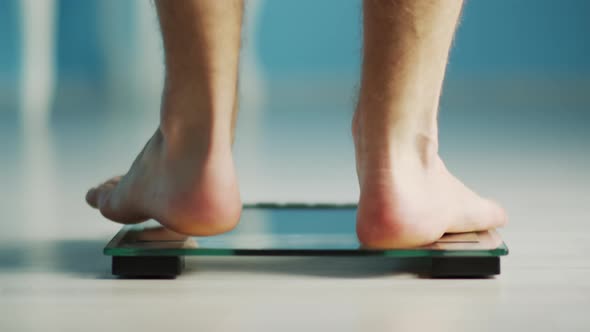 Barefoot male legs, stepping on the scales, weighed and goes, weight loss