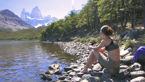 Young woman sitting beside the lake in Laguna Carpi, looking at the Fitz Roy in Patagonia, Argentina