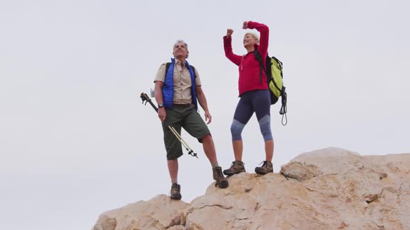 Senior hiker couple with backpack and trekking poles standing with their arms wide open on the rocks