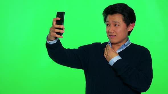 A Young Asian Man Takes a Selfie with a Smartphone - Green Screen Studio