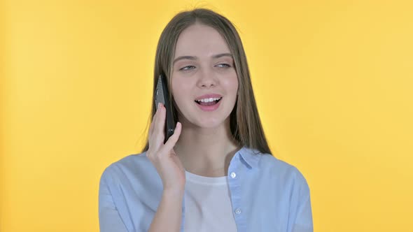 Casual Young Woman Talking on Smartphone, Yellow Background