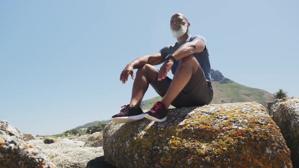 Senior african american man exercising sitting on rocks by the sea