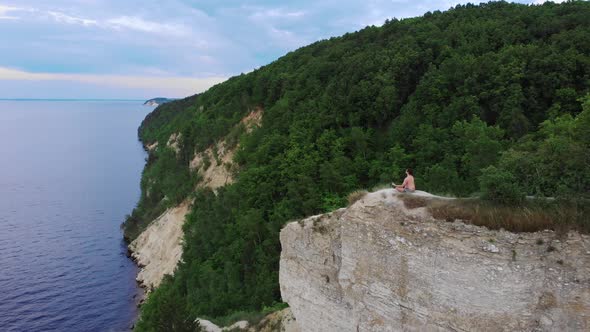 Young Shirtless Man Meditating on a Mountain Around the Forest and River in Early Morning