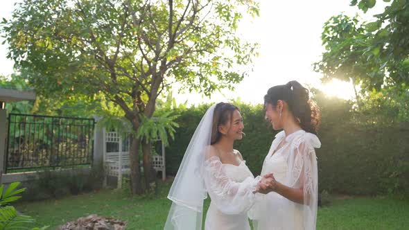 4K Portrait of Asian lesbian couple in wedding dress holding hands walking together in the garden.
