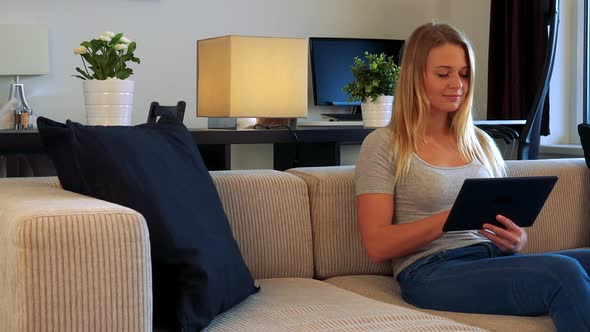 Young Woman Sits on a Couch in a Living Room and Works on the Tablet