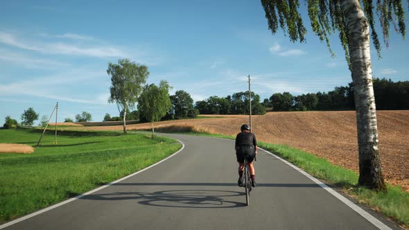 Woman riding bicycle through yellow wheat field and green meadow