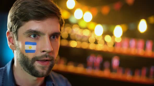 Emotional Argentinian Football Fan With Flag on Cheek Celebrating Team Victory