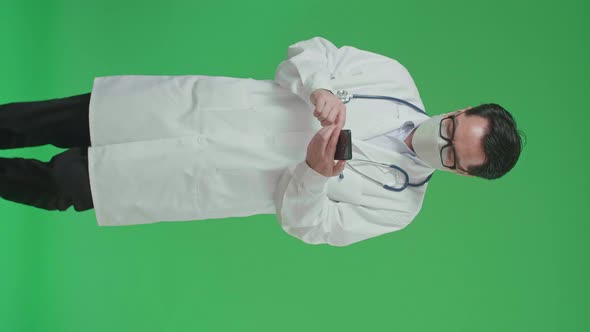 Asian Doctor With Stethoscope Wearing Mask, Using Mobile Phone While Walking On Green Screen