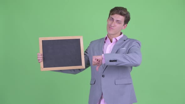 Stressed Young Businessman Holding Blackboard and Giving Thumbs Down