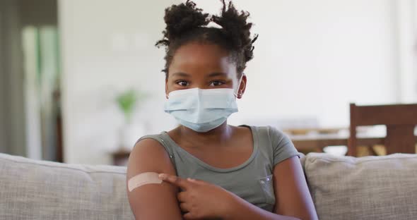 African american girl wearing face mask pointing at bandage on her arm